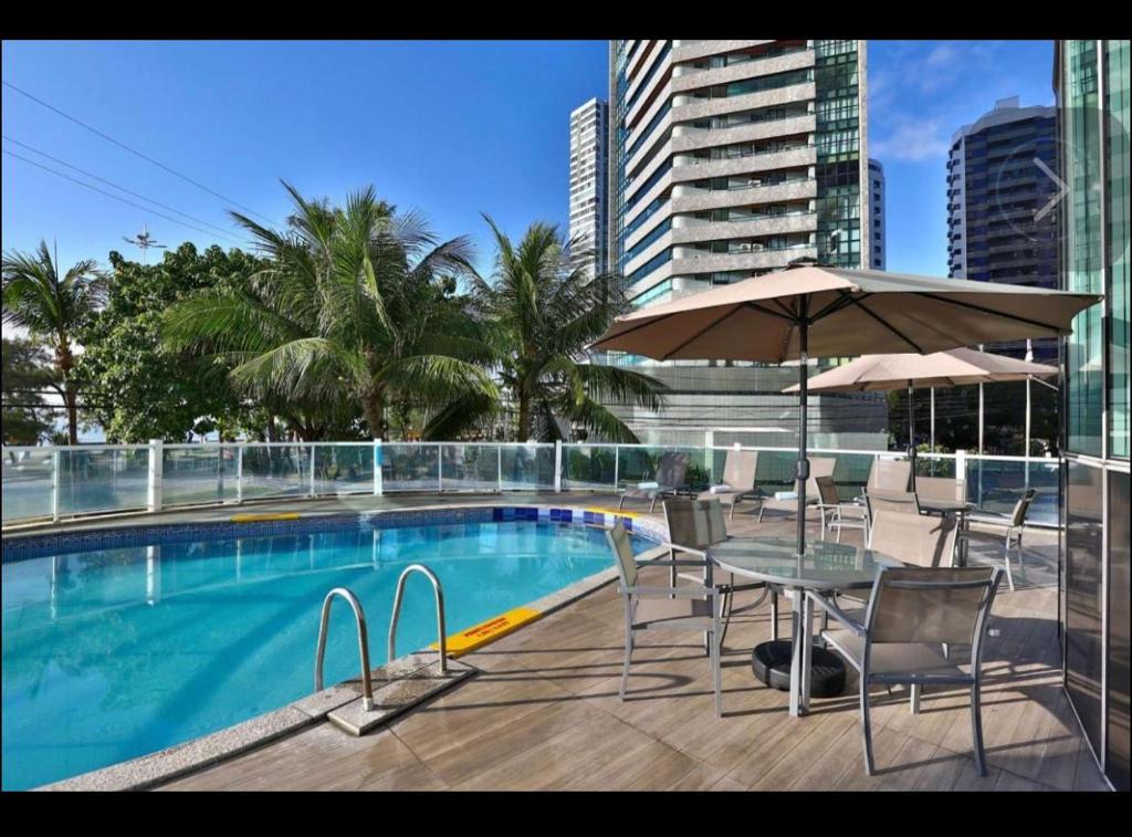 - Piscina con mesa, sillas y sombrilla en Quarto em condomínio beira-mar en Recife