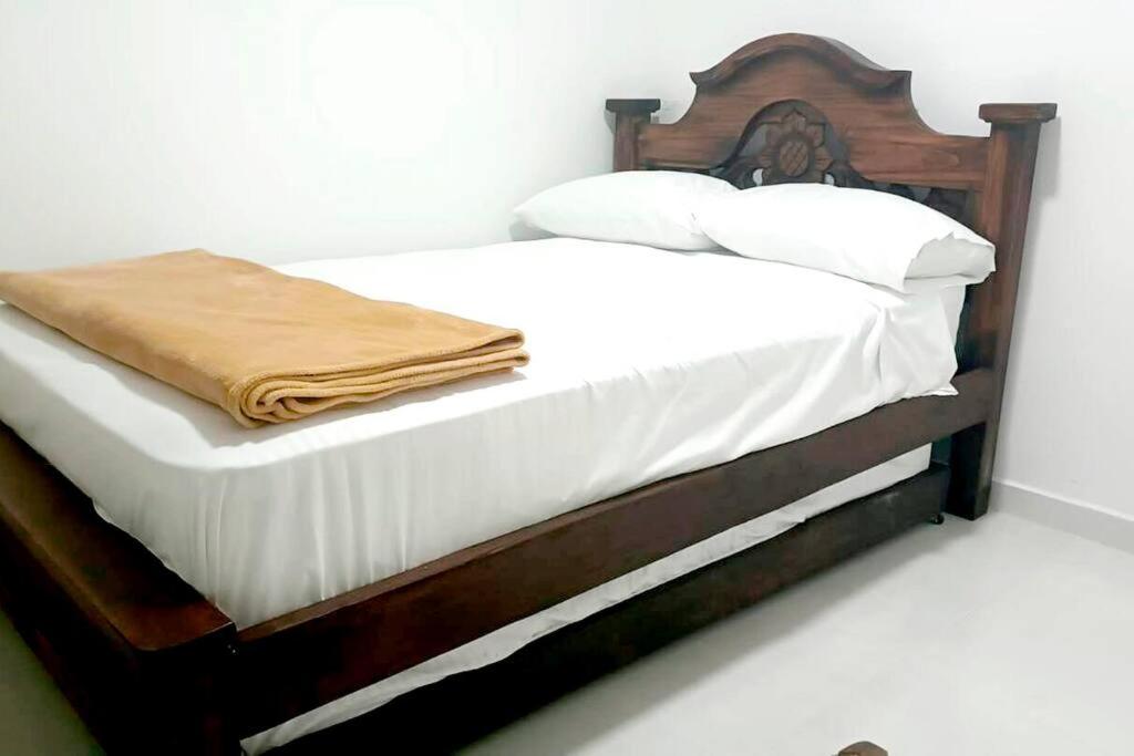 1 cama con marco de madera y sábanas y almohadas blancas en vivienda turistica sara & angel 2, en Salento