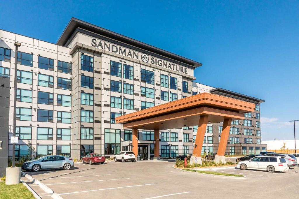 Un gran edificio con coches aparcados en un estacionamiento. en Sandman Signature Saskatoon South Hotel, en Saskatoon
