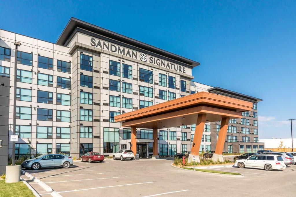 Sandman Signature Saskatoon South Hotel في ساسكاتون: مبنى كبير به سيارات تقف في موقف للسيارات