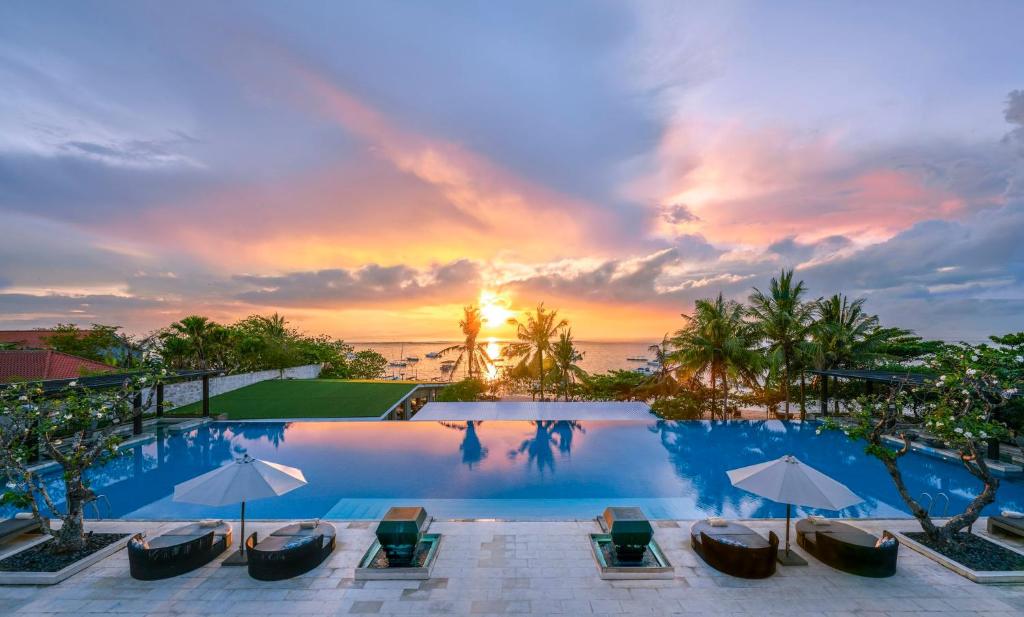 a pool with chairs and umbrellas in front of a sunset at InterContinental Bali Sanur Resort, an IHG Hotel in Sanur