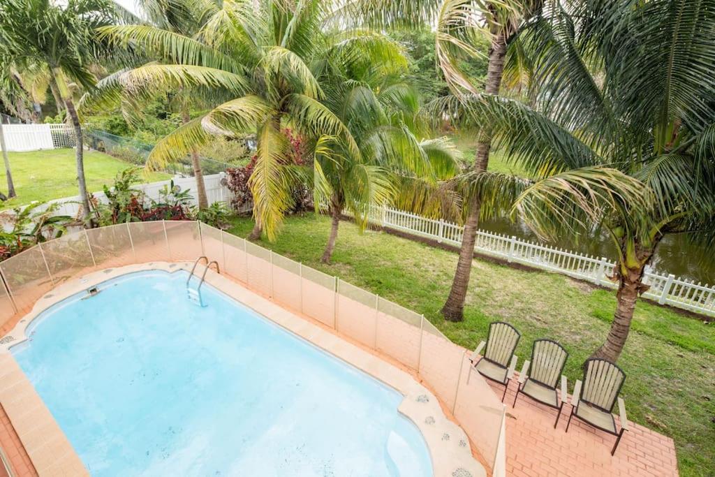 uma piscina com duas cadeiras e palmeiras em Waterfront 2-Story Villa with Heated Pool em Pembroke Pines