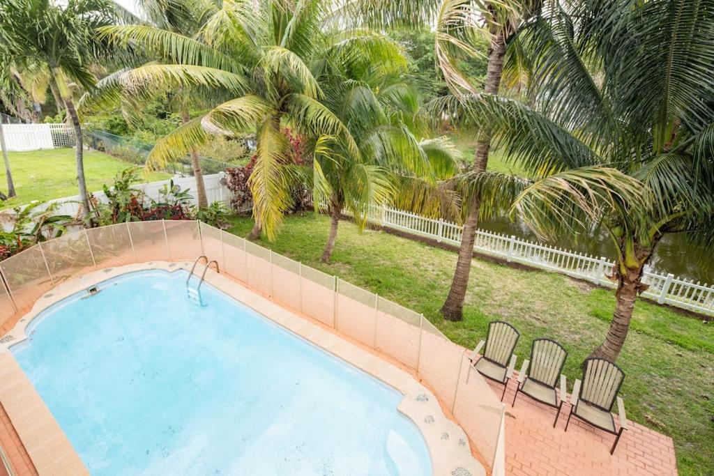a swimming pool with two chairs and palm trees at Waterfront 2-Story Villa with Heated Pool in Pembroke Pines