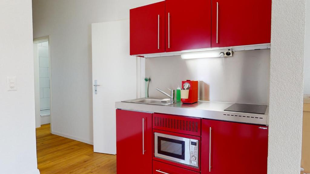 a kitchen with red cabinets and a microwave at Anstatthotel Affoltern am Albis - self-check-in in Affoltern