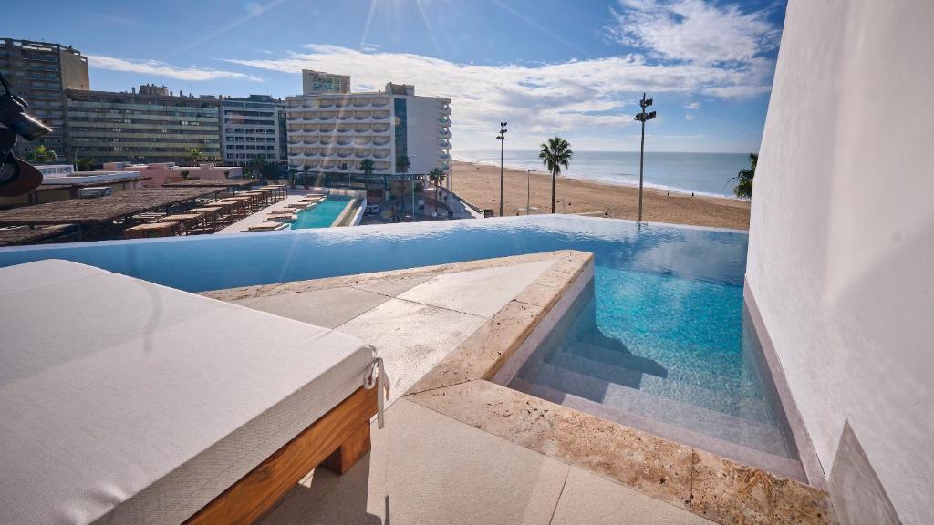 a swimming pool on the roof of a building with a beach at Cádiz Bahía by QHotels in Cádiz