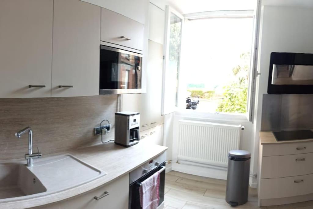 kuchnia z białymi szafkami, umywalką i oknem w obiekcie Suresnes : 2 pièces cosy w mieście Suresnes