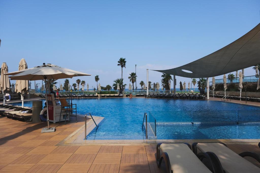 una gran piscina con sillas y sombrilla en Dan Panorama Tel Aviv Hotel, en Tel Aviv