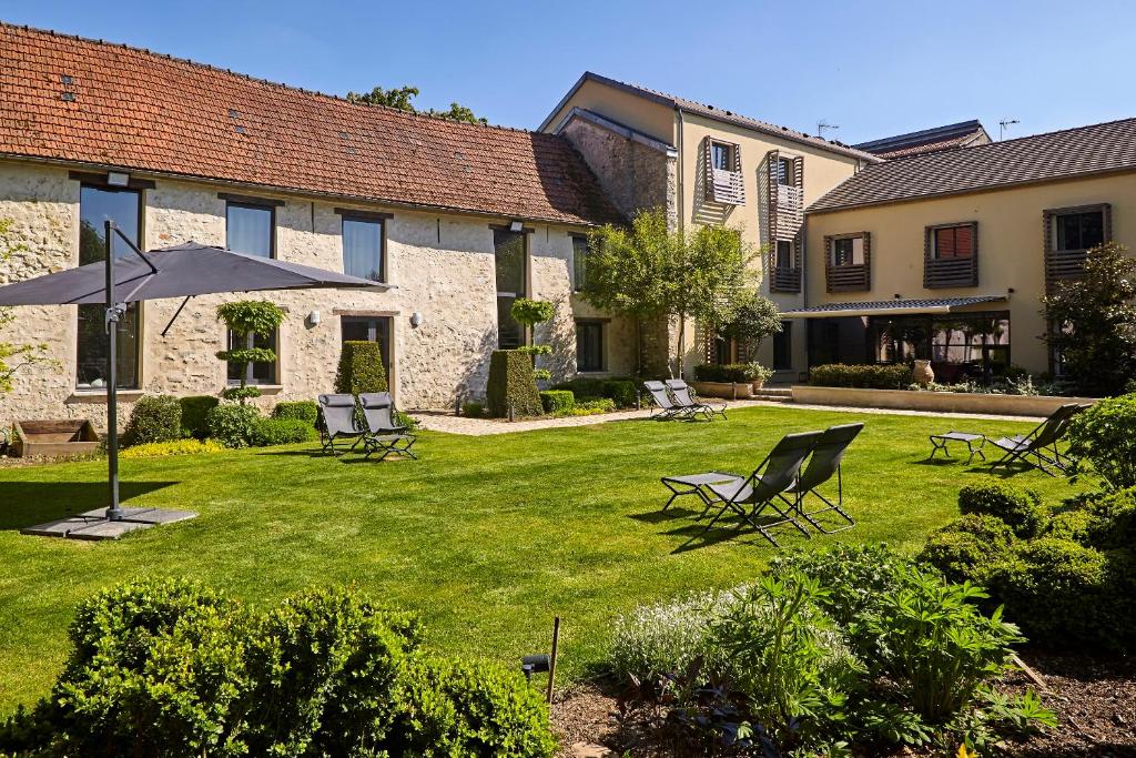 un patio con sillas y una sombrilla frente a un edificio en Chambre d'hôtes Les Herbes Folles, en Mauregard