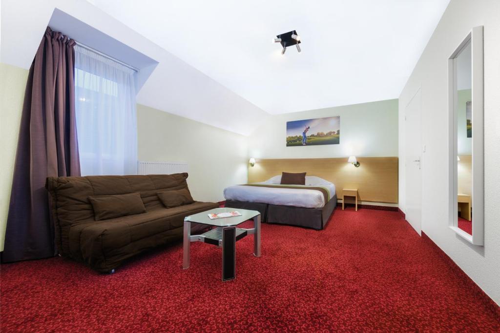 a hotel room with a couch and a bed at The Originals City, Hôtel Acadine, Le Neubourg (Inter-Hotel) in Le Neubourg