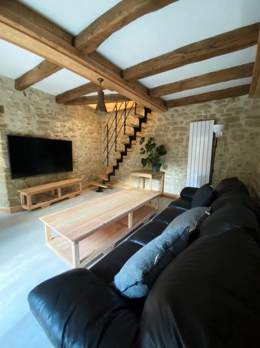 a living room with a black leather couch and a tv at Gîte : La vieille bâtisse. in La Baume-Cornillane
