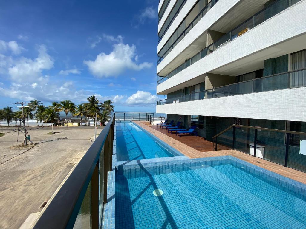 a swimming pool next to a building with a beach at Residencial SAN MARINO BEIRA MAR in Ilhéus