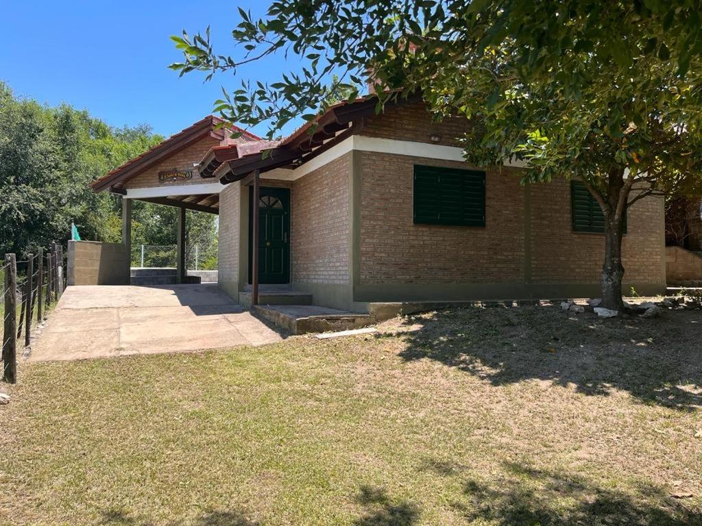 una pequeña casa de ladrillo con un árbol delante de ella en El sueño de mama en Santa Rosa de Calamuchita