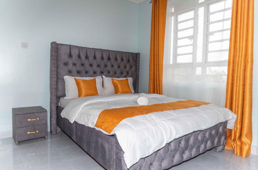 ein Schlafzimmer mit einem großen Bett mit orangefarbenen Vorhängen und einem Fenster in der Unterkunft Springstone executive apartment Rm 15 in Langata Rongai