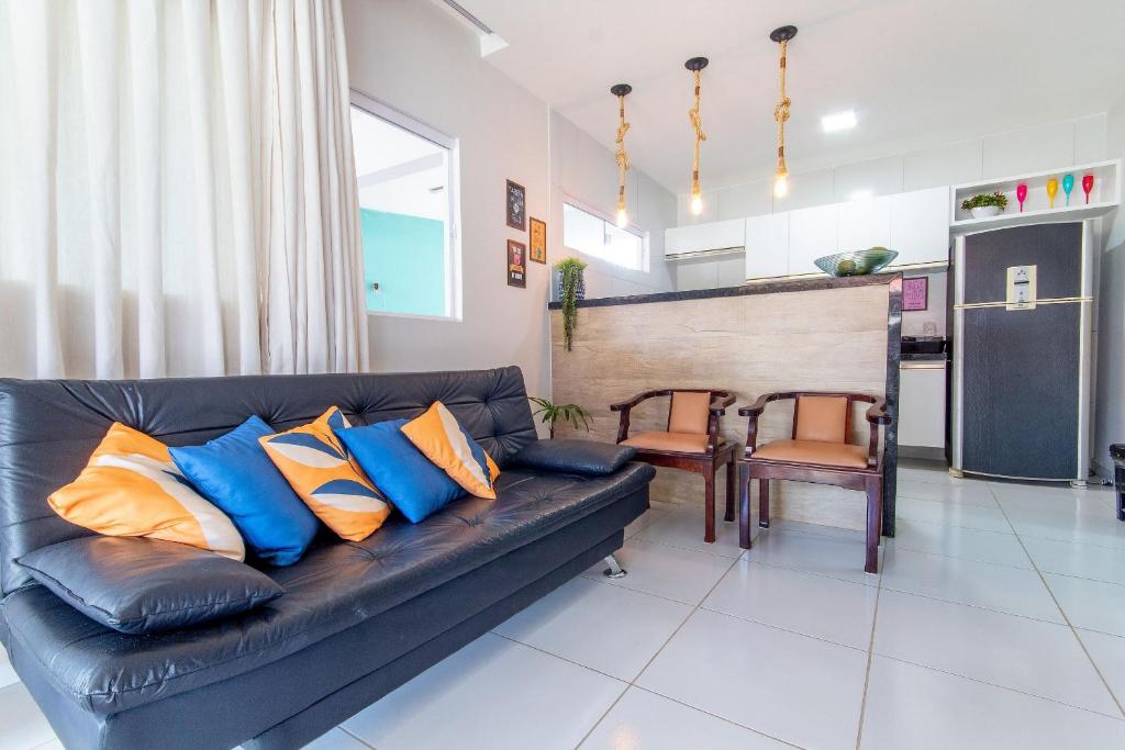 a living room with a black leather couch with blue and orange pillows at Incrível casa na praia de Camurupim por Carpediem in Nísia Floresta