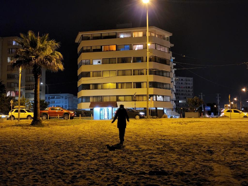 un homme marchant sur une plage la nuit avec un bâtiment dans l'établissement Avenida del Mar , Primera Linea, edificio Canto del agua, à La Serena