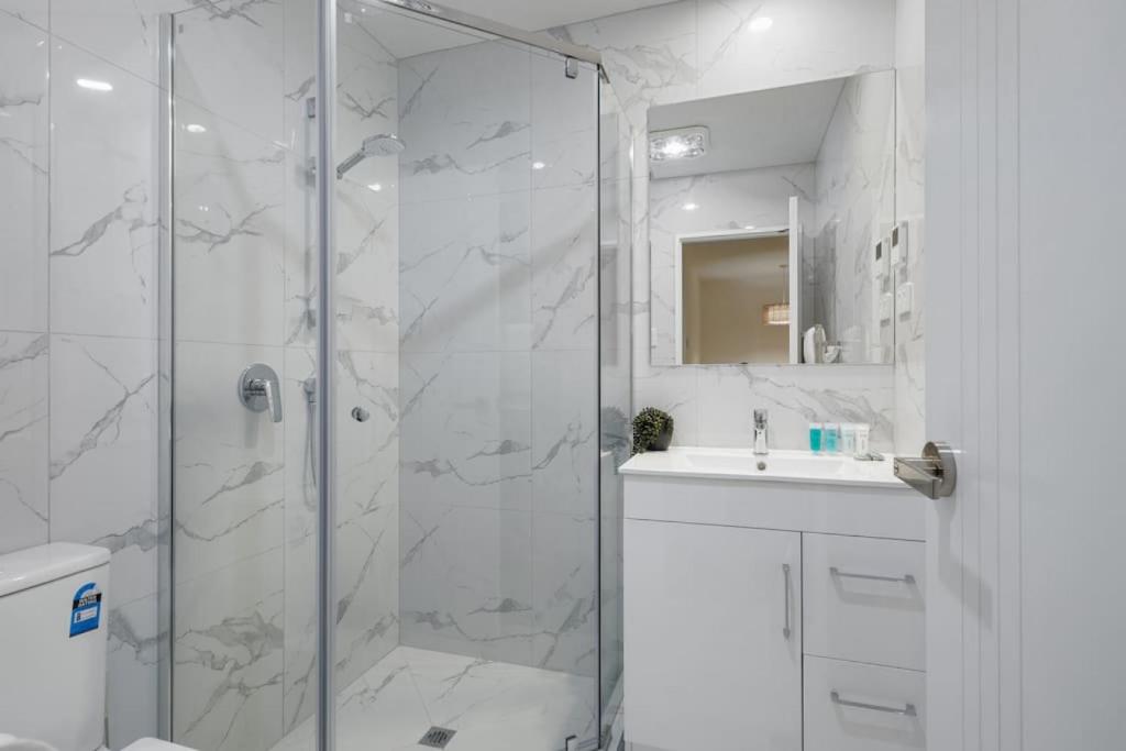 a white bathroom with a shower and a sink at 3 Bdrm Mangere Delight - Parking - Wi-Fi - Netflix in Auckland