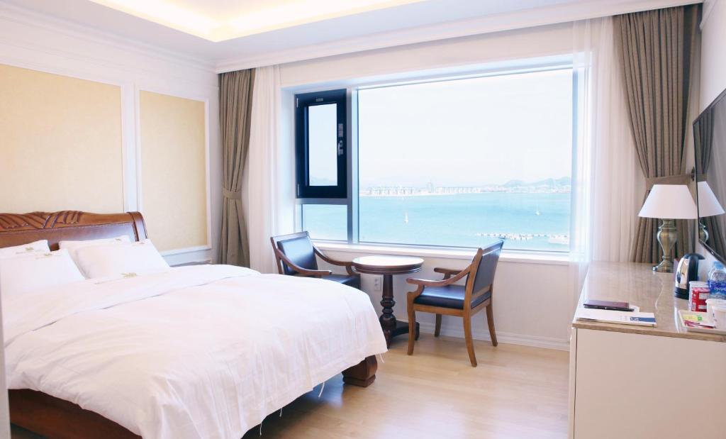een slaapkamer met een bed, een bureau en een groot raam bij Fontana Beach Hotel in Mokpo
