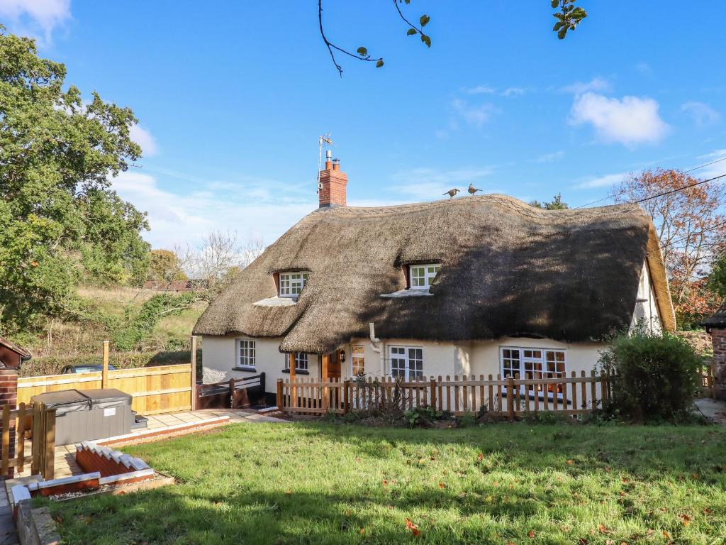 Una casa de campo con techo de paja y una valla delante de ella en Posbury Lodge, en Crediton