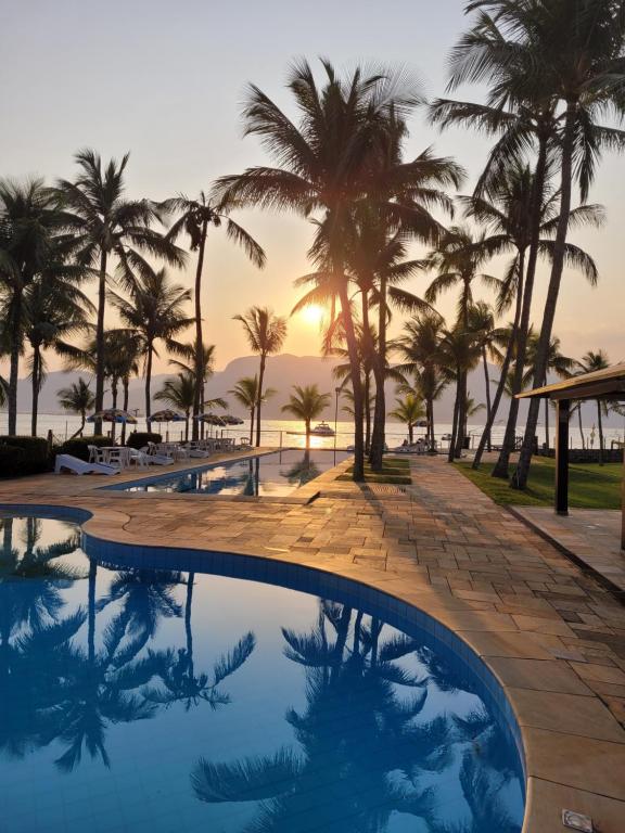 a pool with palm trees and a sunset in the background at Pousada Casa Amarela in Ilhabela