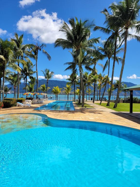 a pool with palm trees and the ocean in the background at Pousada Casa Amarela in Ilhabela