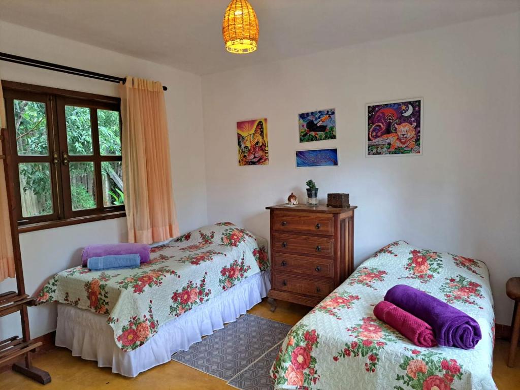 a bedroom with two beds and a dresser and a window at Suite Solteiro Cristal Rosa, Suites Ananda in Alto Paraíso de Goiás