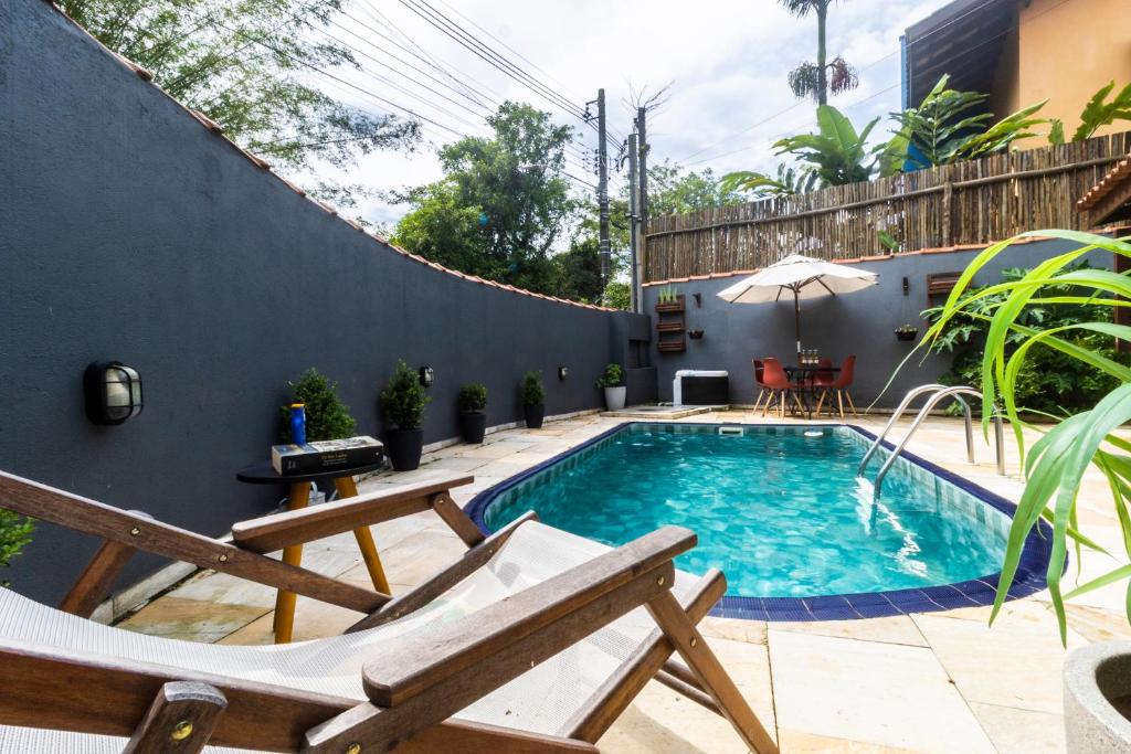 uma piscina com duas cadeiras e um guarda-sol em Casa Charmosa com Piscina em Barra do Una em Barra do Una