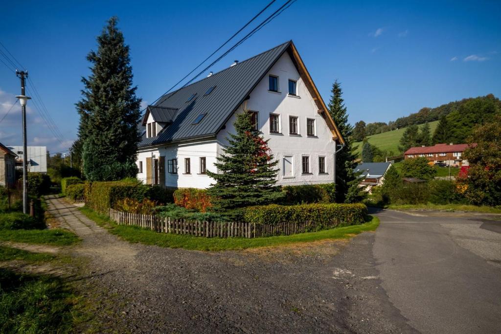 een wit huis met een zwart dak op een straat bij Penzion Pod Sudem in Lázně Libverda