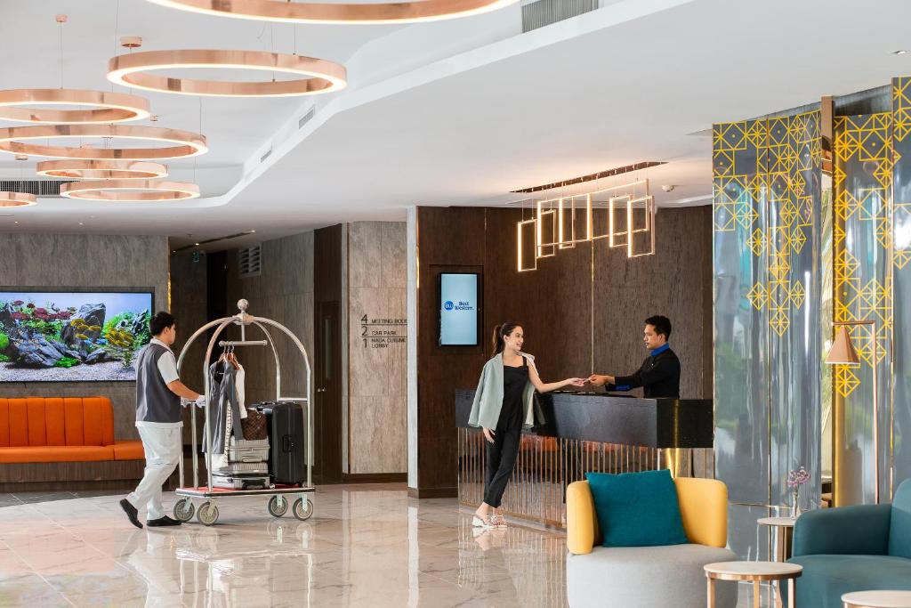 Reception staff assist a guest in a polished lobby with luggage seating and decorative lighting.