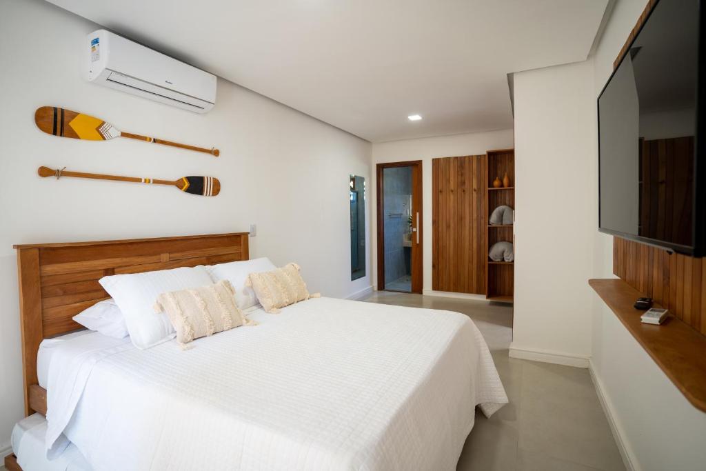 PARAÍSO DO DENDÊ - FLATS في بارا غراندي: غرفة نوم بيضاء فيها سرير وتلفزيون