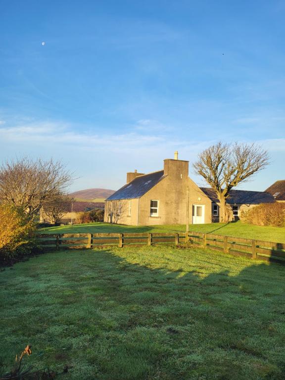 a house with a fence in front of a field at Kirbister Mill Farm Cottage in Kirkwall