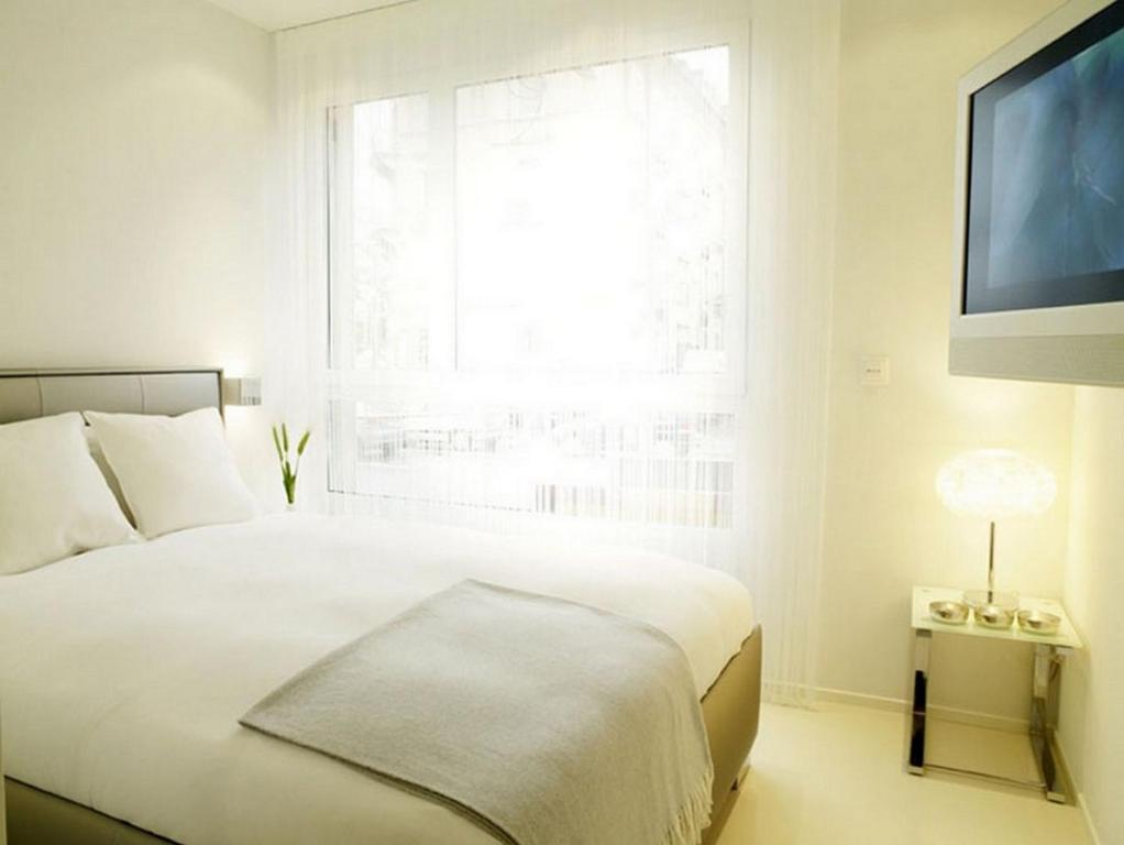 a white bedroom with a bed and a large window at VISIONAPARTMENTS Binzmühlestrasse 48 - contactless check-in in Zurich