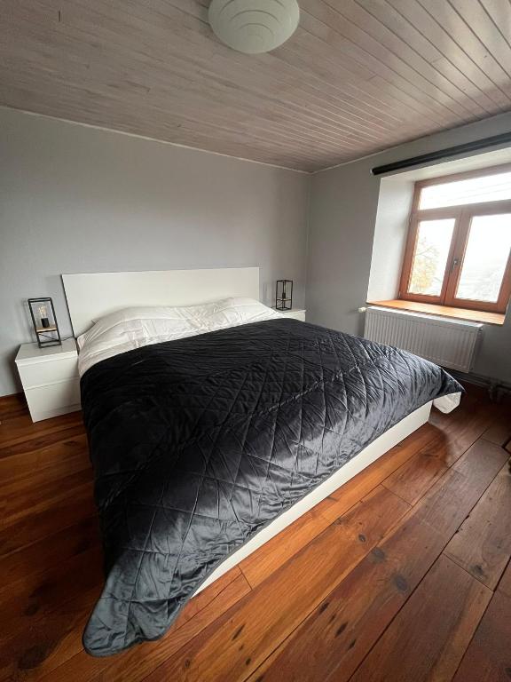 a bedroom with a bed with a black comforter and a window at Gîte Les trois charmes in Gouvy