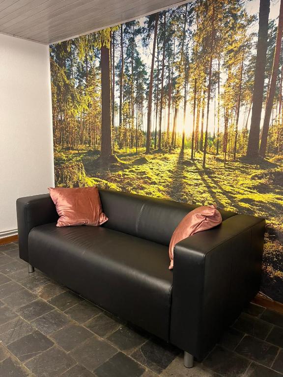 a black couch in a room with a forest mural at Gîte Les trois charmes in Gouvy