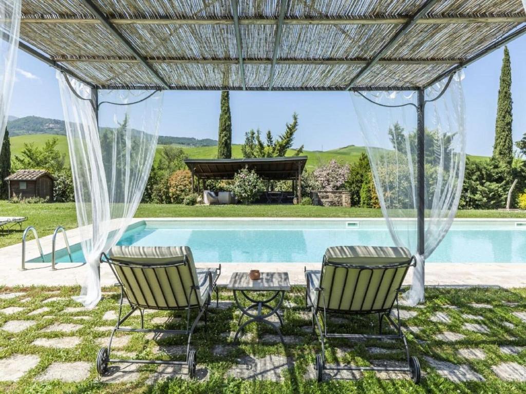 een patio met 2 stoelen en een tafel naast een zwembad bij Cozy Villa in Castiglione D'orcia Italy with Private Pool in Castiglione dʼOrcia
