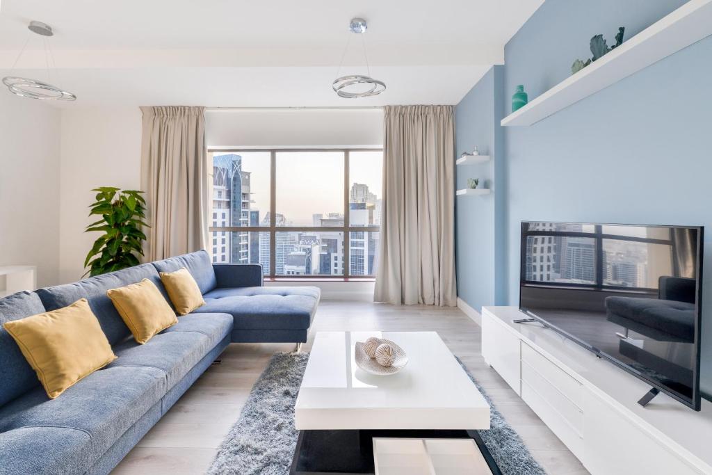 ein Wohnzimmer mit einem blauen Sofa und einem TV in der Unterkunft Luxury JBR · Marina View · 5* Beach Resorts Access in Dubai