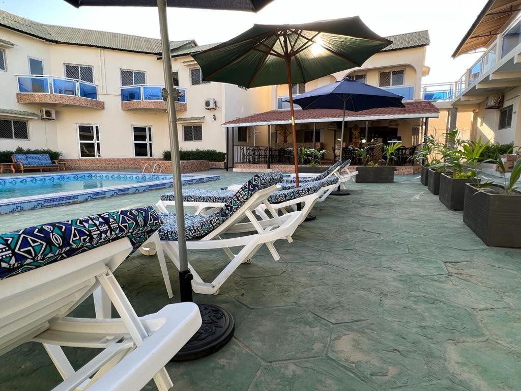 uma fila de espreguiçadeiras com um guarda-sol ao lado de uma piscina em TRANQUIL RESORT HOTEL em Brusubi