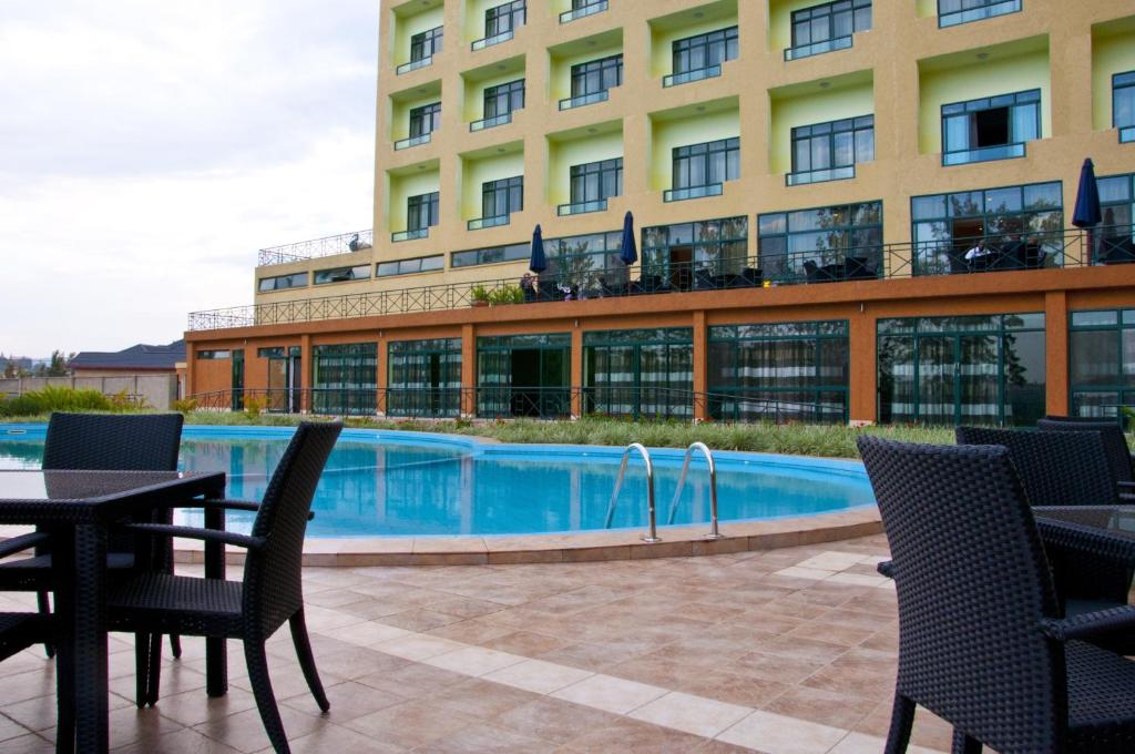 un patio del hotel con mesas y sillas y una piscina en Gorillas Golf Hotel, en Kigali