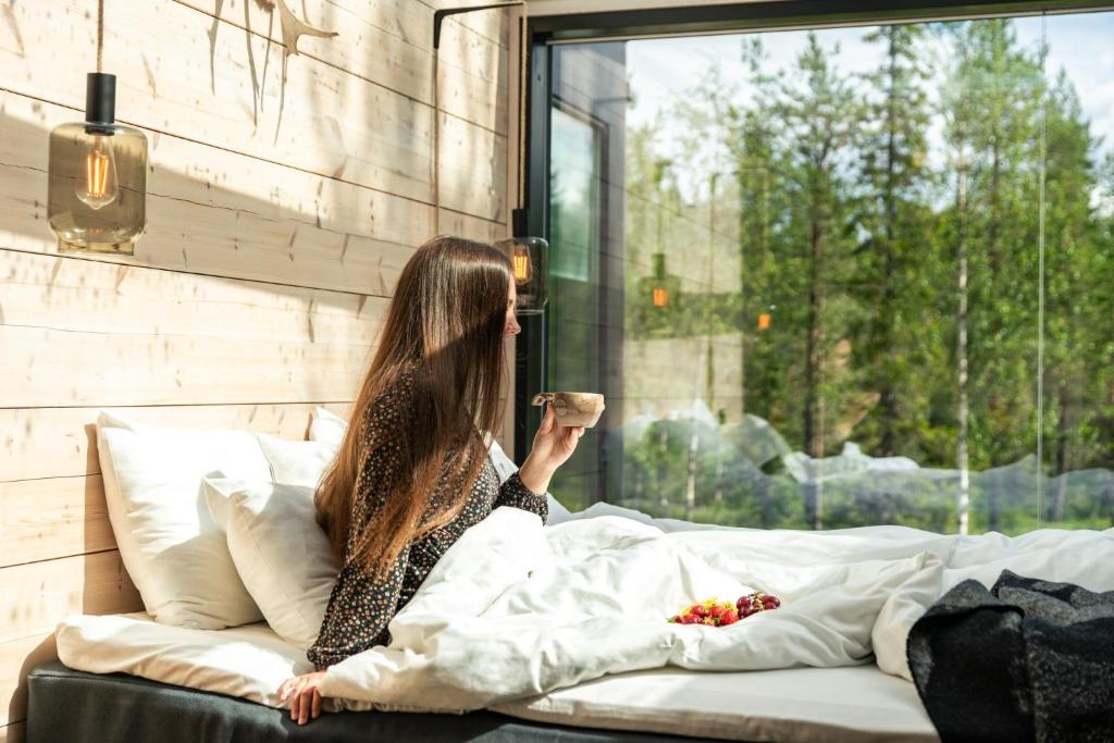 una mujer sentada en una cama mirando por la ventana en Kuuru Tunturilaakso by Kide Hotel, en Syöte