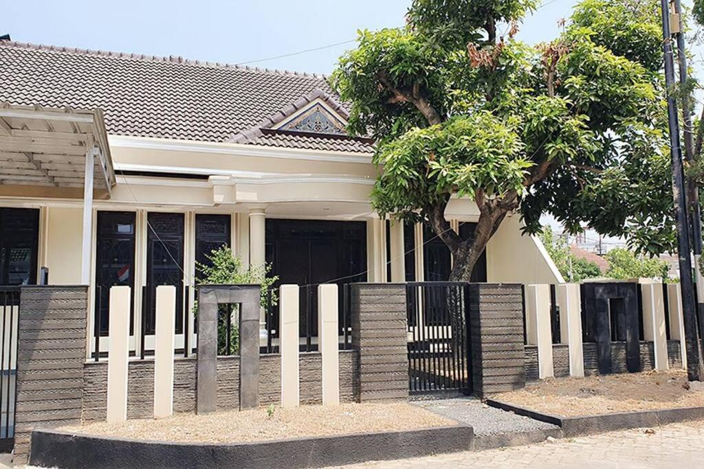 une clôture blanche devant une maison avec un arbre dans l'établissement Villa 5 BR utk Family/Grup di Villa Citra, Lampung, à Tanjungkarang