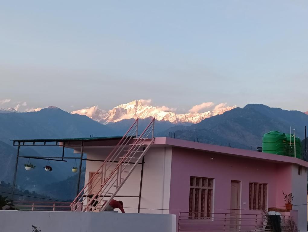 un edificio rosa con una escalera en el techo con montañas en Kedar View Homestay en Ukhimath