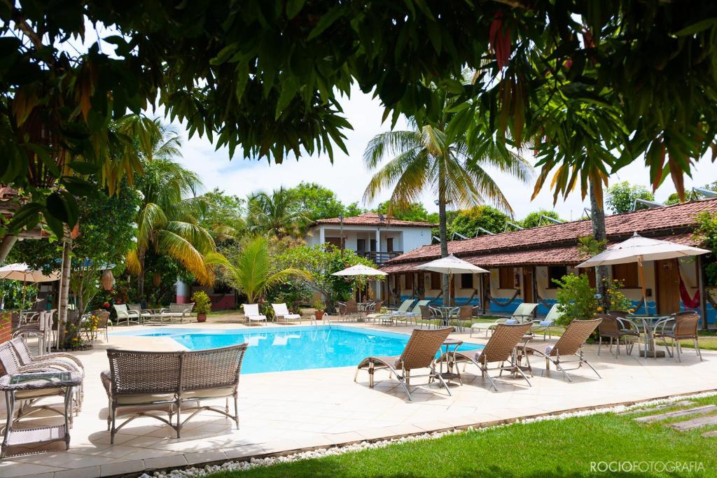 einen Pool in einem Resort mit Stühlen und Sonnenschirmen in der Unterkunft Pousada Estalagem Vila Tania in Itaúnas
