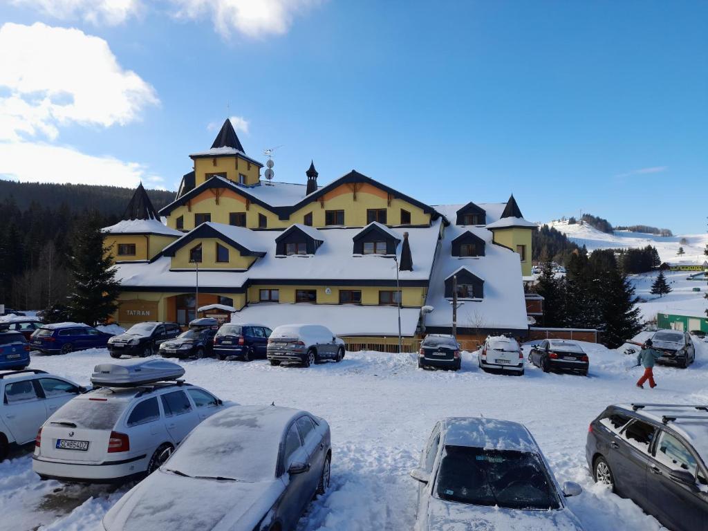ein großes Gebäude mit Autos im Schnee in der Unterkunft Podkrovný apartmán Donovaly AD Tatran in Donovaly