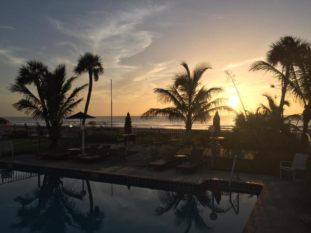 a pool with palm trees and the ocean at sunset at Surf Studio Beach Resort in Cocoa Beach