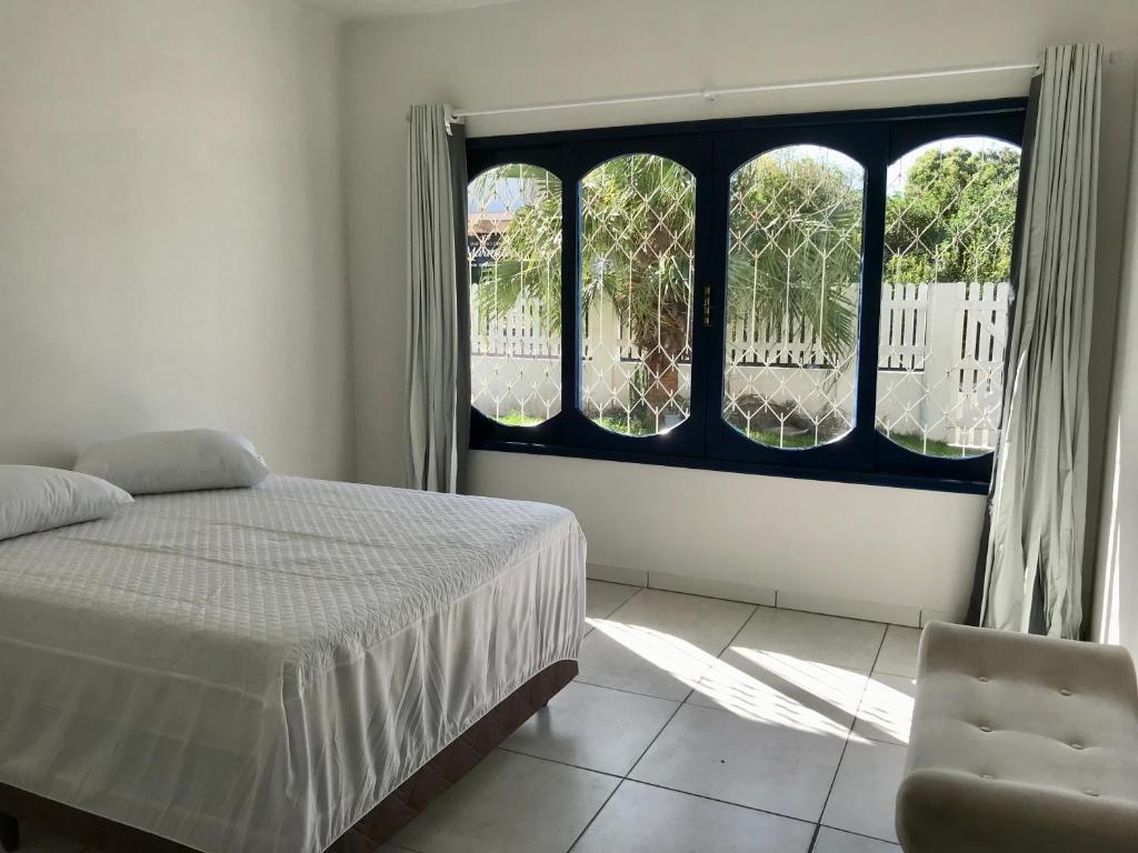 1 dormitorio con cama, ventana y silla en Residencial Casa da Vila apto 3, en Imbituba