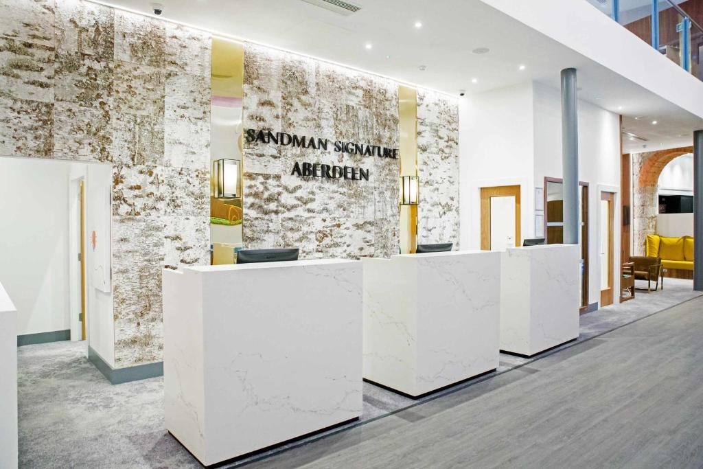 a lobby with white reception desks and a stone wall at Sandman Signature Aberdeen Hotel & Spa in Aberdeen