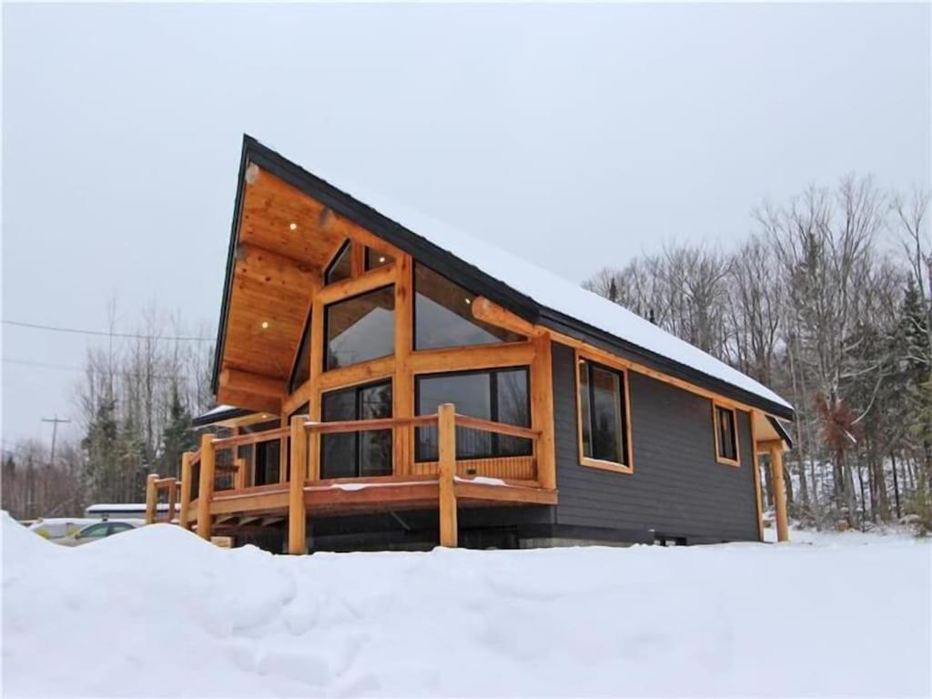 una cabaña de madera en la nieve con nieve alrededor en Le Billot- Chalet Rustic avec Spa, en Saint-Philémon
