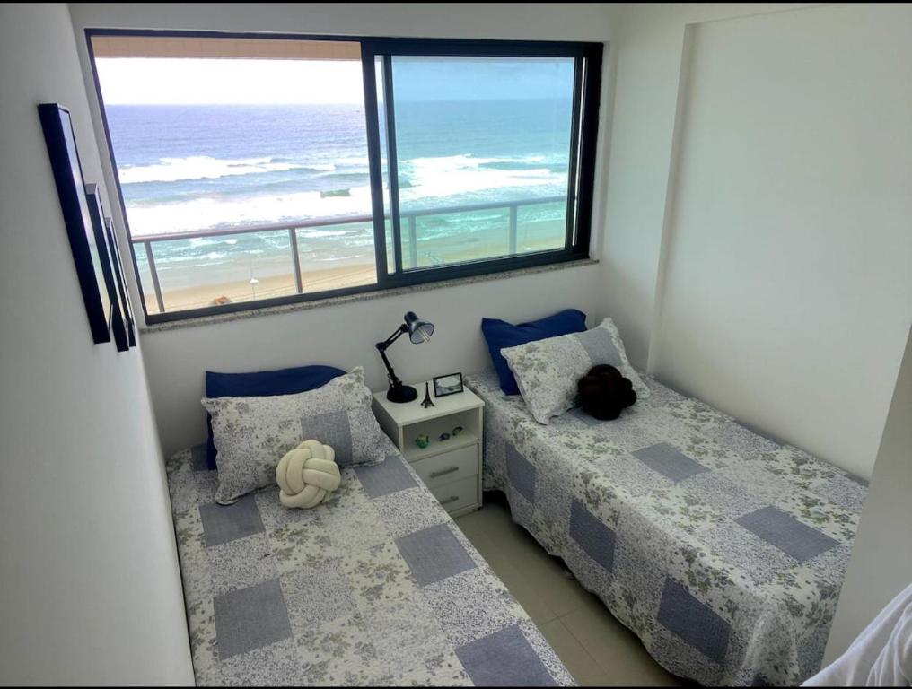a bedroom with two beds and a view of the ocean at Salvador - Praia do Flamengo - Pé na areia in Salvador
