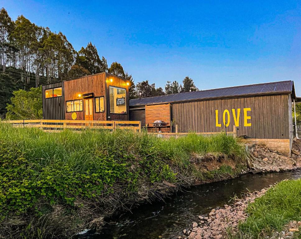 a house with the word love written on it next to a river at Shepherd & Sprout Boutique Tiny House - Cradle Country in Wilmot