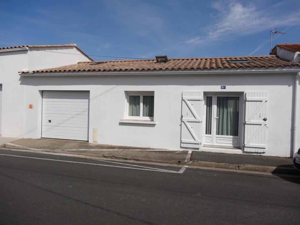 une maison blanche avec deux portes de garage dans une rue dans l'établissement Maison confortable, proche plages et centre, 4 pers, terrasse, wifi, centre L'Aiguillon-sur-Mer - FR-1-476-11, à LʼAiguillon-sur-Mer