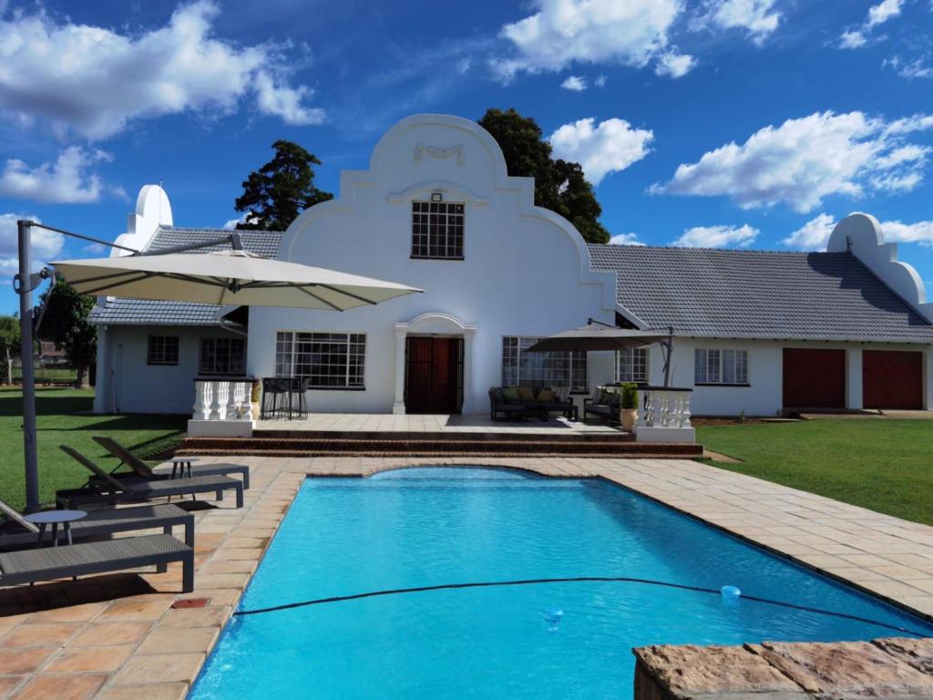 a villa with a swimming pool in front of a house at Blackwood Eco Lodge in Witbank